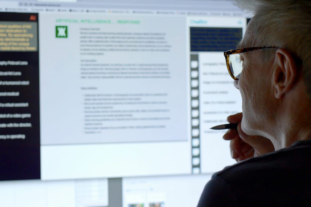 Stock image showing a mature man’s face looking into a large computer screen as type is being added to the screen by an Artificial intelligence, AI, chatbot.