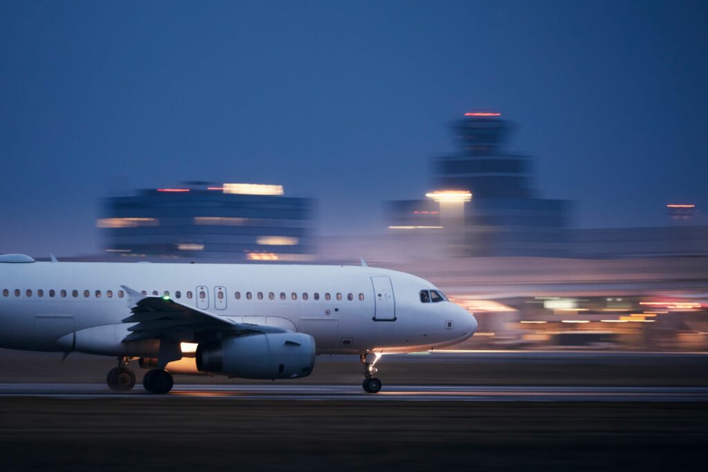 Airplane during take off on airport runway at night against air traffic control tower