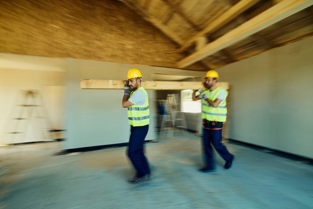 Manual workers cooperating while carrying wood plank at construction site.