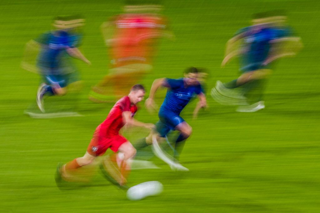 Male football players challenging for ball on field during match, blurred motion.