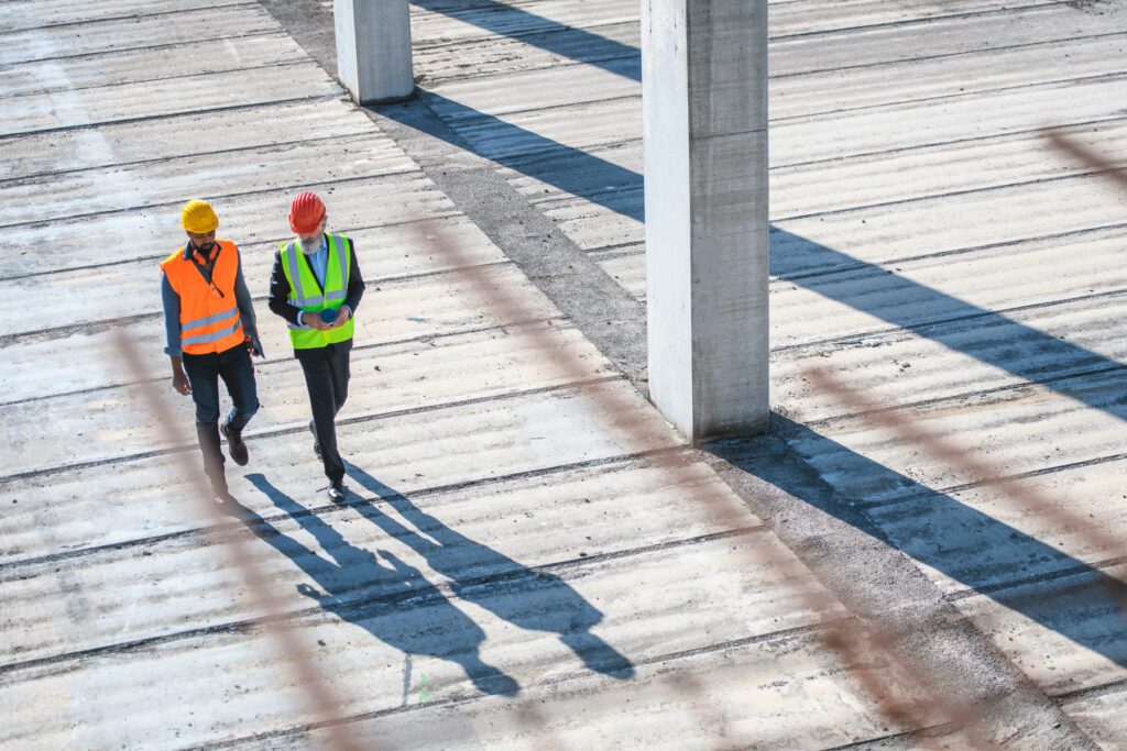 Elevated view through defocused rebar in foreground of construction site foreman and manager walking and talking.