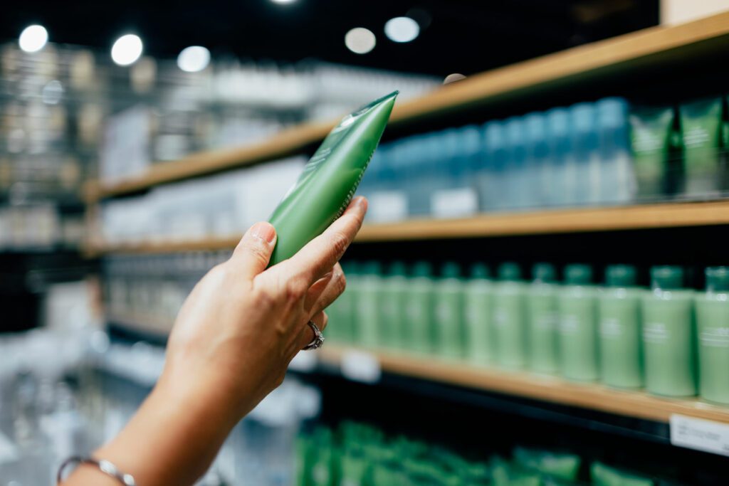 A cropped photo of a woman holding a tube of a hand cream while shopping at a store