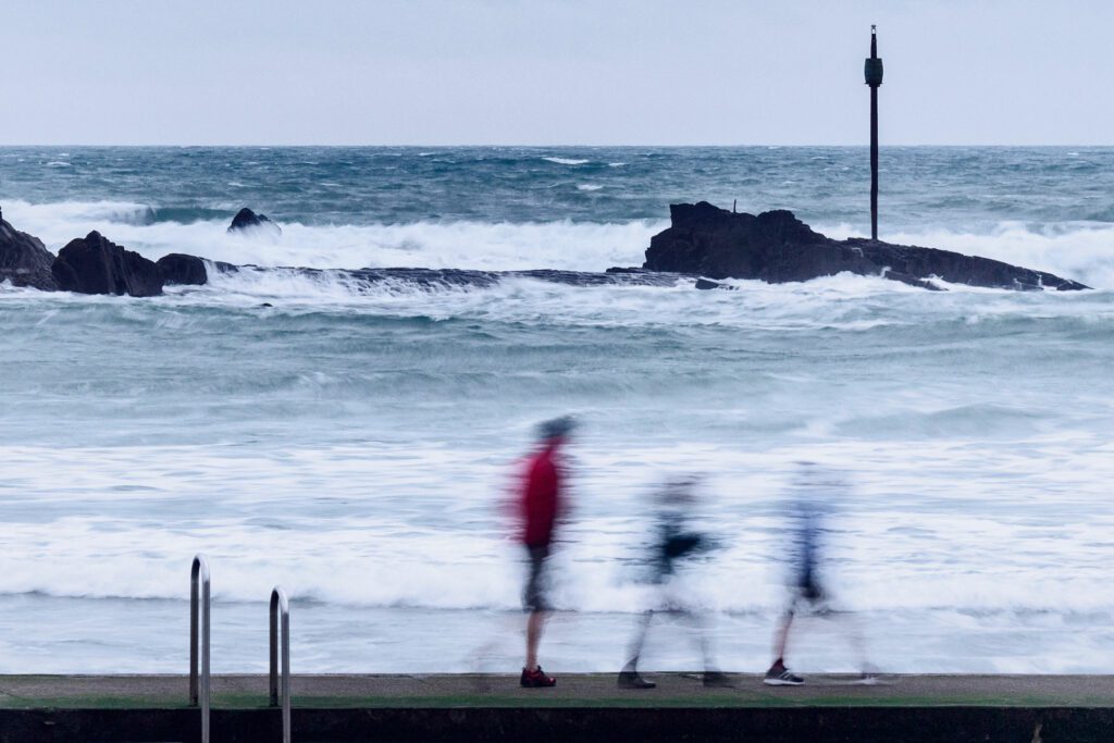 Waves break over the hidden rocks and beat against the shore as family walk along beach.