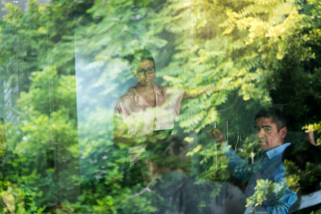 A photo of young businesswoman giving presentation seen through glass window.